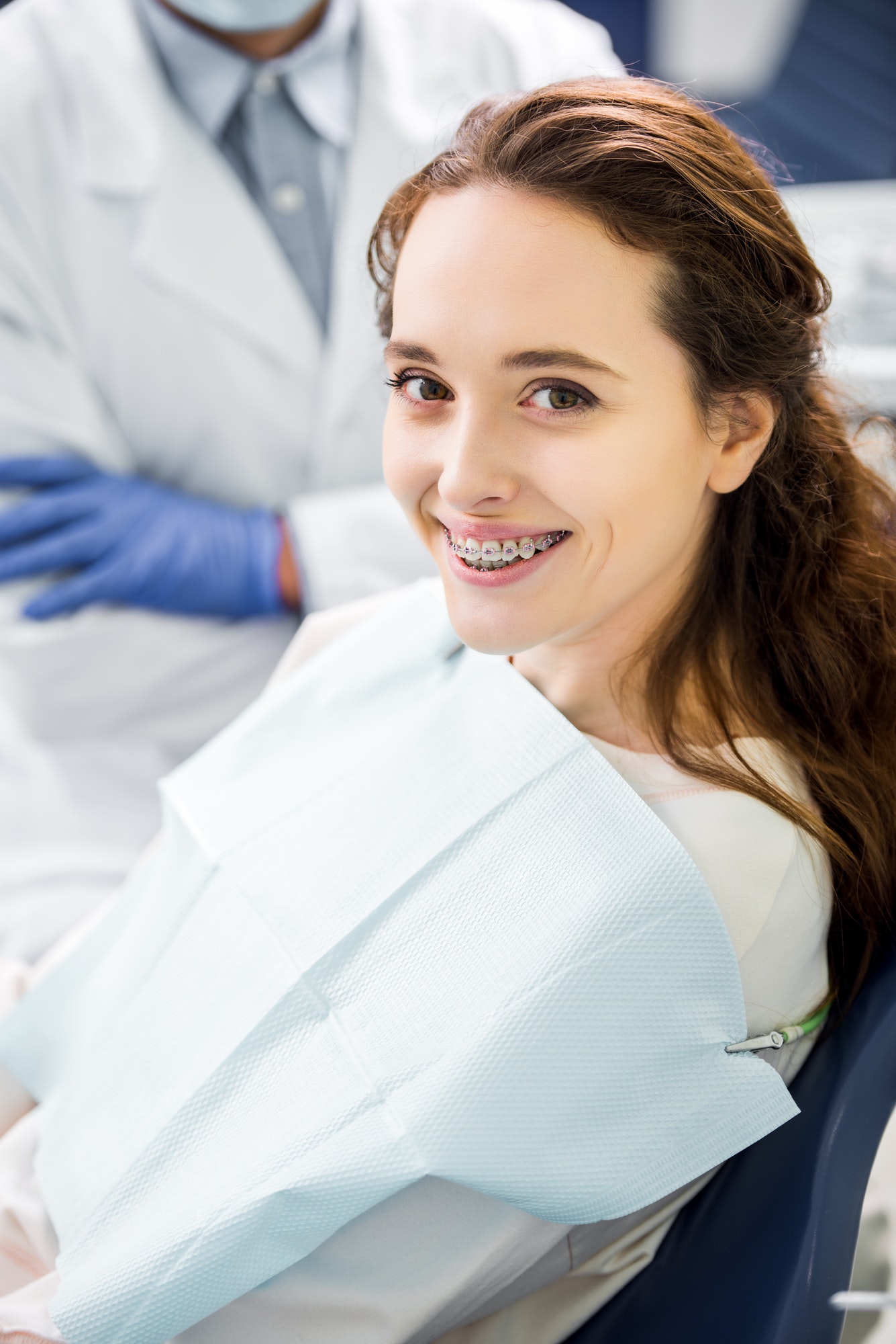 selective focus of woman in braces smiling with dentist standing with crossed arms on background